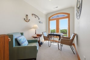 A cozy living room with a green sofa, a dining table with chairs, a lamp, and decorative wall art. - Spacious 5BR Corolla retreat with private pool, hot tub, and game room. (Corolla)