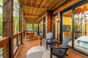 A wooden deck with a table and chairs, a grill, and a view of the forest. - Mountain-Modern Blue Ridge Retreat with Sauna, Hot Tub & Year-Round Views (Blue Ridge)