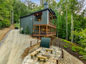A cabin with a stone deck, wooden benches, and a fire pit. - Mountain-Modern Blue Ridge Retreat with Sauna, Hot Tub & Year-Round Views (Blue Ridge)