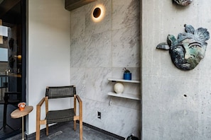A seating area with a chair and a small table, a wall-mounted shelf with decorative items, and a wall-mounted light fixture. - Gallery-Style Loft, Workspace & Prime Location (Mexico City)