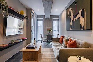 A modern living room with a sofa, coffee table, and a TV mounted on the wall. - Combo Suites: 4BR, Gym, Rooftop & Coworking (Mexico City)