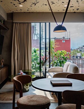 A modern interior with a round table, chairs, a sofa, and a view through large windows. - Combo Suites: 4BR, Gym, Rooftop & Coworking (Mexico City)