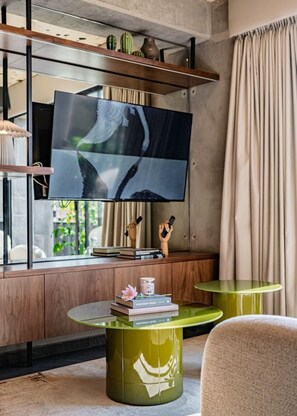 A modern living room with a flat-screen TV mounted on a wooden wall, a green glass coffee table, and a comfortable chair. - Combo Suites: 4BR, Gym, Rooftop & Coworking (Mexico City)