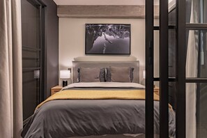 Et moderne hotelværelse med en seng, et natbord, en lampe og et billede i ramme på væggen.
