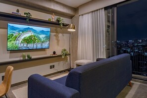 A modern living room with a flat-screen TV, a sofa, a floor lamp, and a city view through large windows. - Boutique 1BR Suite Near Reforma (Mexico City)