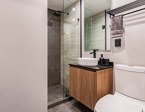 Et moderne badeværelse med en glasbrusekabine, en hvid vask og et toilet.
