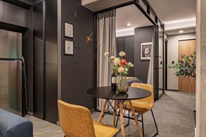Et moderne interiør med spiseområde, et rundt bord, to stole, et køleskab og en dør med træpanel.