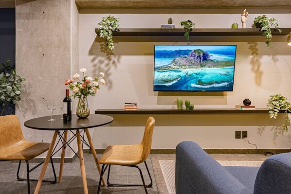 En moderne stue med et fladskærms-tv på væggen, et rundt bord med stole og en sofa.