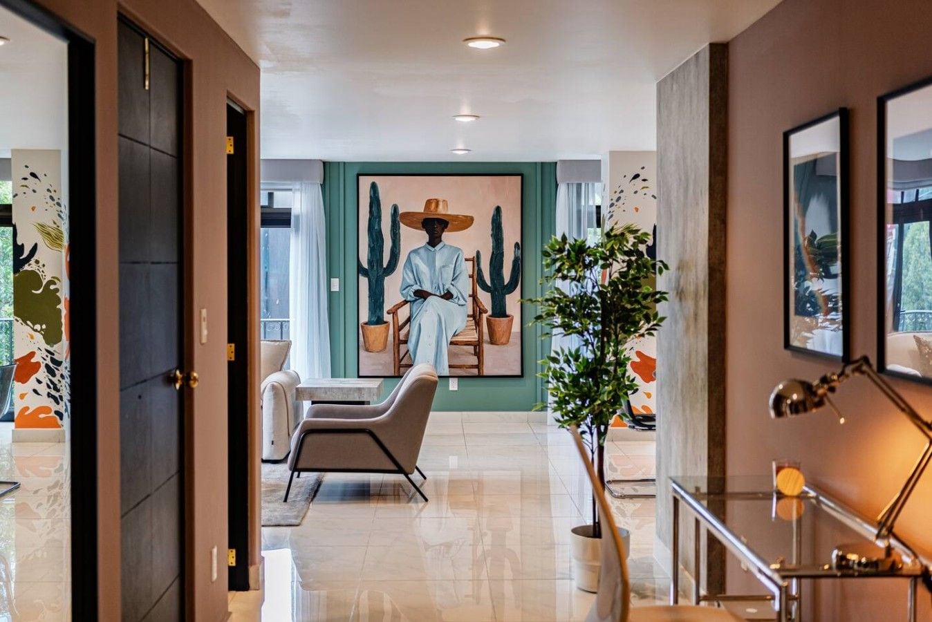 A modern hotel lobby with a seating area, a large cactus painting, and a staircase.
