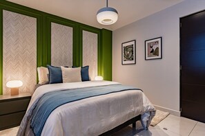 A bedroom with a bed, two bedside lamps, a green accent wall, and two framed pictures on the wall. - Balsas Urban Escape | Near Reforma (Mexico City)