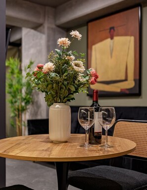 Ein runder Holztisch mit Blumen in einer Vase, zwei Weingläsern und einer Weinflasche.