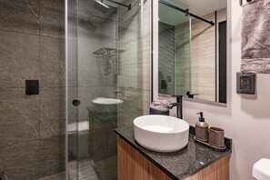 Ein modernes Badezimmer mit einer gläsernen Duschkabine, einem runden Waschbecken und einem großen Spiegel.