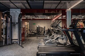 Uma academia com esteiras, aparelhos de musculação e um suporte para agachamentos.