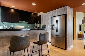 A modern kitchen with a large stainless steel refrigerator, two bar stools, and a green backsplash. - Serene CDMX Stay | Modern (Mexico City)