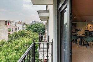 A balcony with a view of greenery and buildings, a dining area with chairs and a table, and a modern interior with a sofa and a vase. - Serene CDMX Stay | Modern (Mexico City)