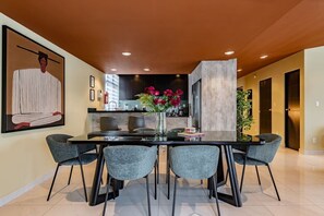 A dining area with a glass table and grey chairs, a vase with flowers, and a painting on the wall. - Serene CDMX Stay | Modern (Mexico City)