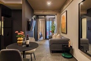 Un salon moderne avec un canapé, une table à manger ornée d’un vase de fleurs, une bouteille de vin et un téléviseur.