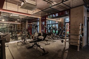 Ein Fitnessstudio mit unterschiedlichen Trainingsgeräten, großen Fenstern und einem Betonboden.