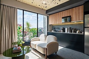 A modern living room with a sofa and a coffee table, a kitchen with a microwave and coffee machine, and a large window with a view of the city. - Designer Loft | Rooftop, Gym & Workspace (Mexico City)