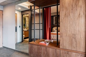 A hotel room with a wooden cabinet, a bed with a red curtain, and a view into the bathroom. - Designer Loft | Rooftop, Gym & Workspace (Mexico City)