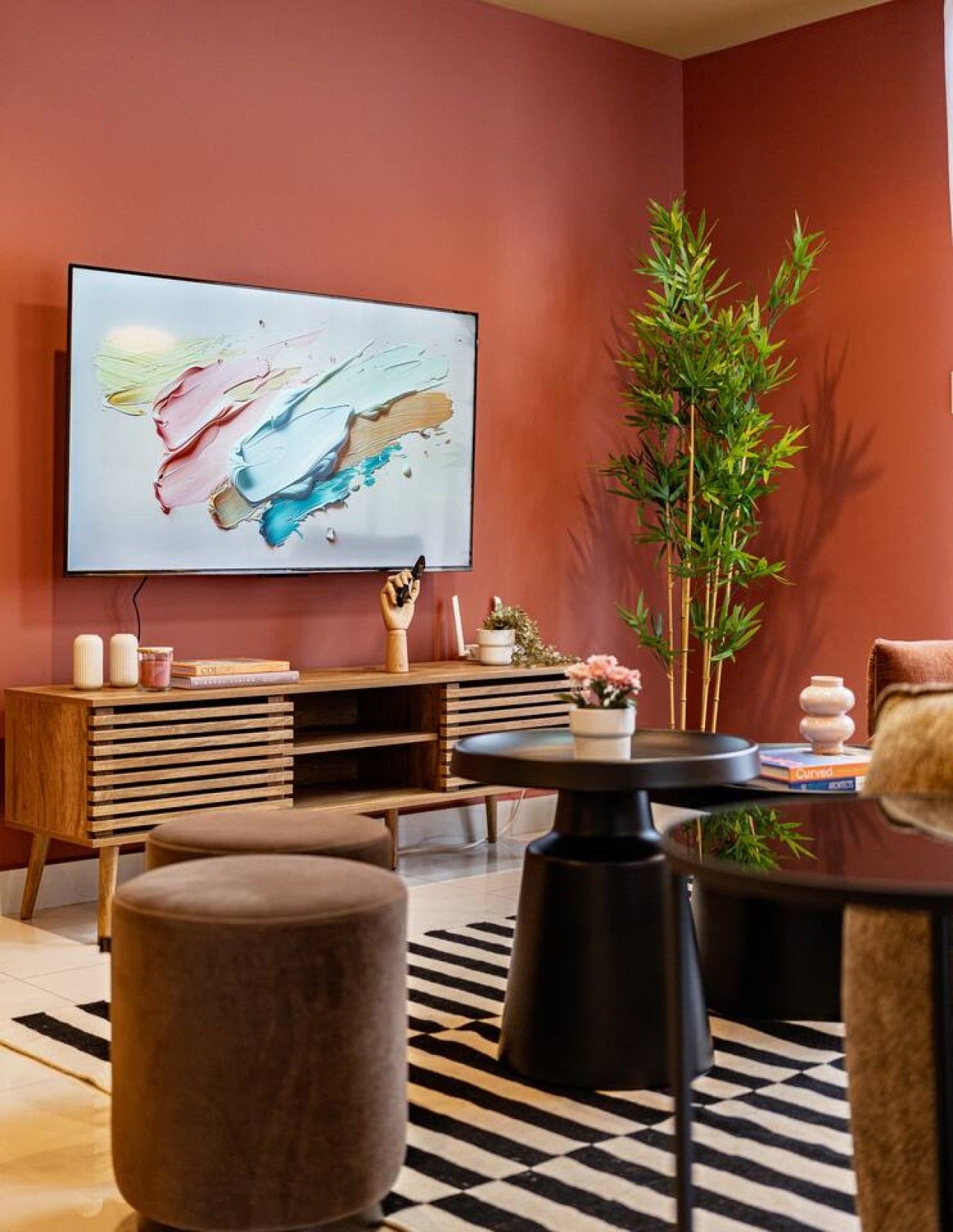 A modern living room with a flat-screen TV, a tall bamboo plant, a round coffee table, and a patterned rug.