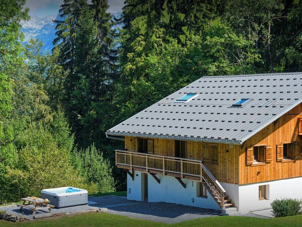 A cabin with a wooden exterior, a balcony, and a hot tub in the foreground.