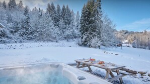 Paisagem coberta de neve com banheira de hidromassagem e mesa de piquenique.