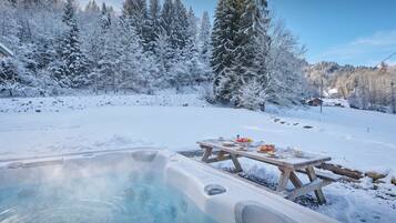 A snow-covered landscape with a hot tub and picnic table.