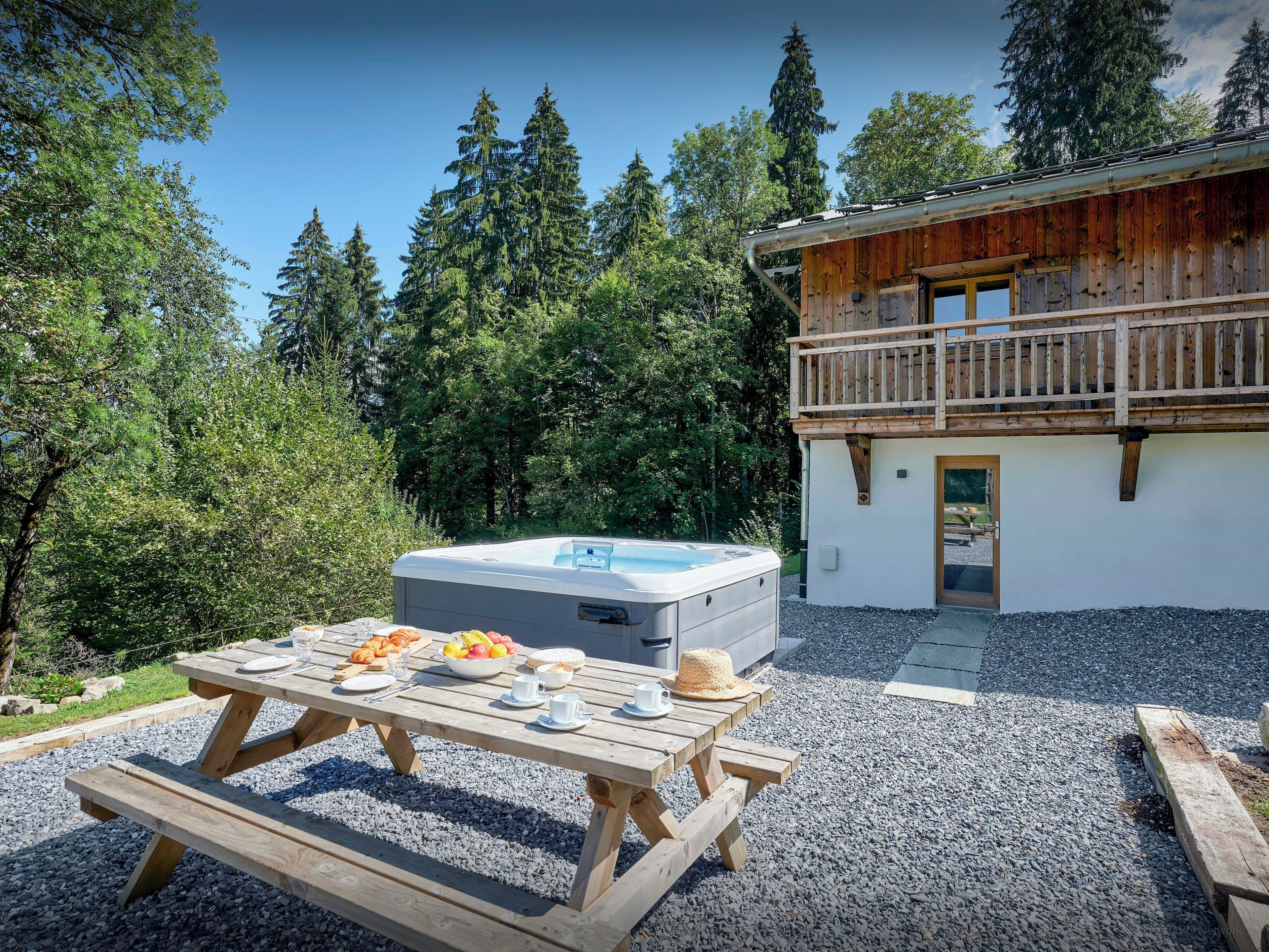 A wooden cabin with a hot tub and a picnic table set up outside.