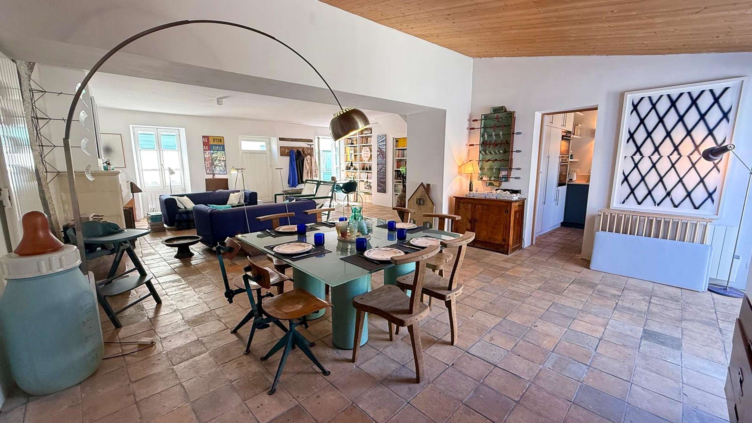 A spacious living area with a dining table, chairs, a sofa, and a kitchen in the background.