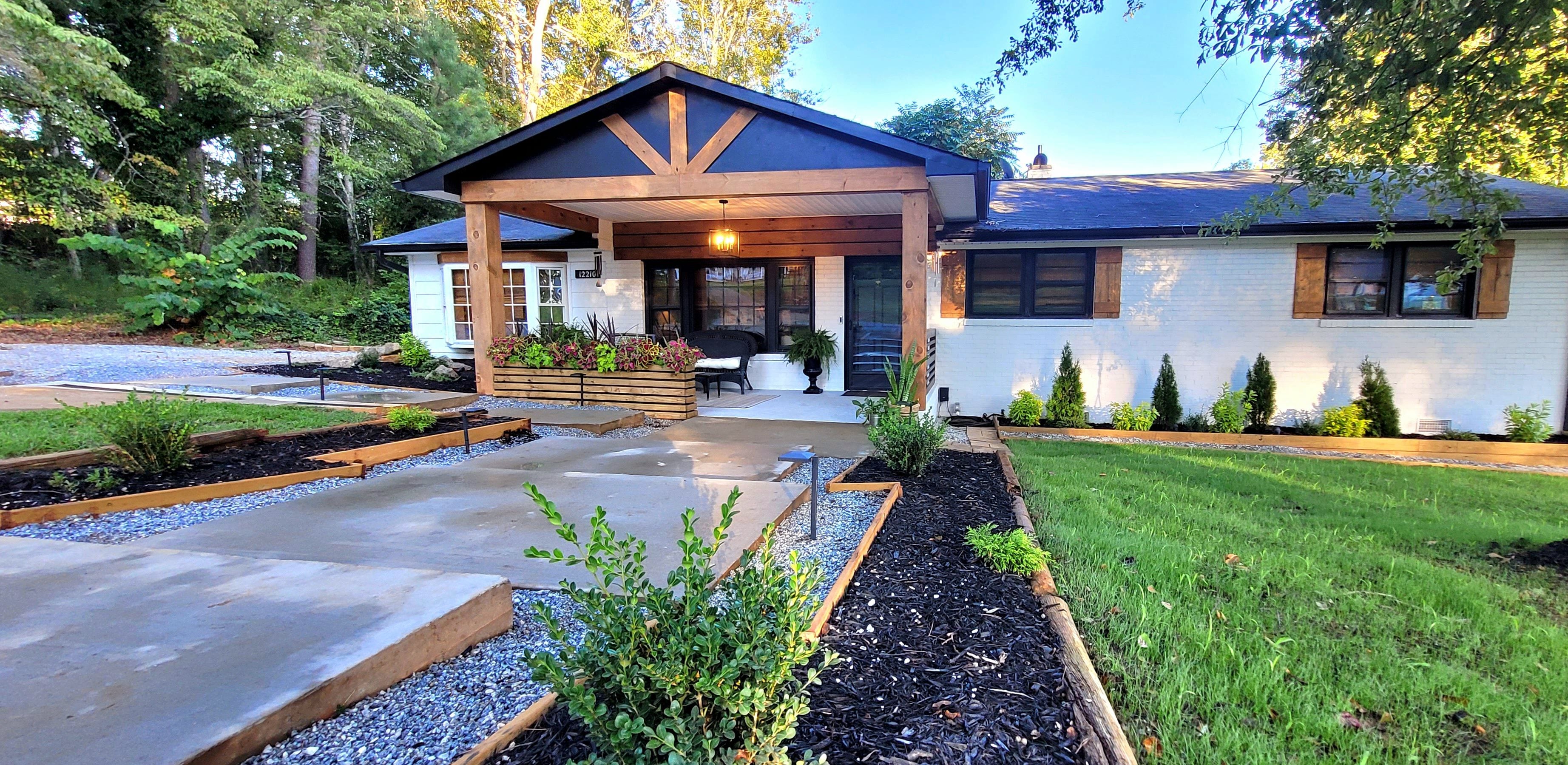 A residential property with a covered porch, a front yard with raised beds, and a well-maintained lawn.