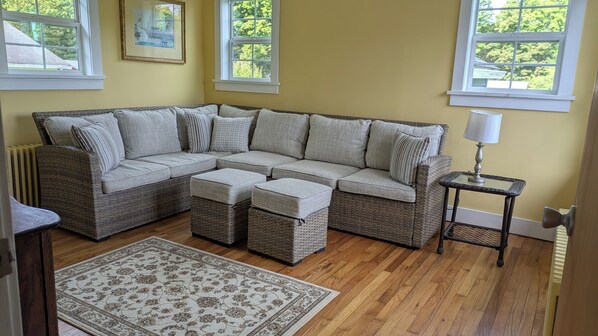 A sectional sofa with matching ottomans, a small table with a lamp, and a patterned rug on a wooden floor.