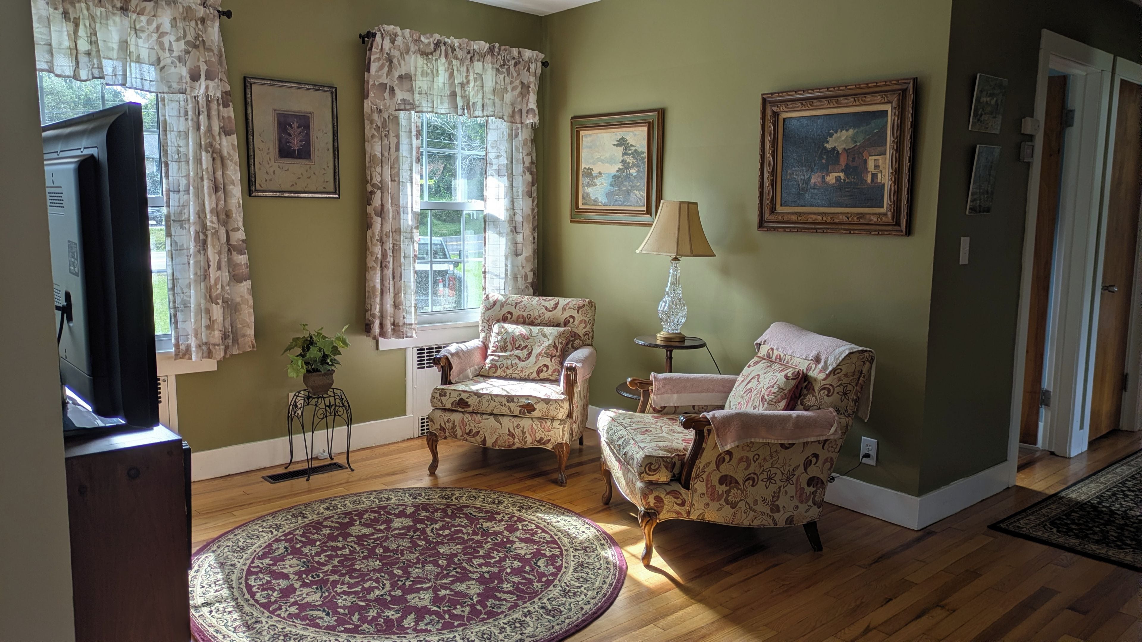 A living room with two armchairs, a round rug, a lamp, and framed artwork on the walls.