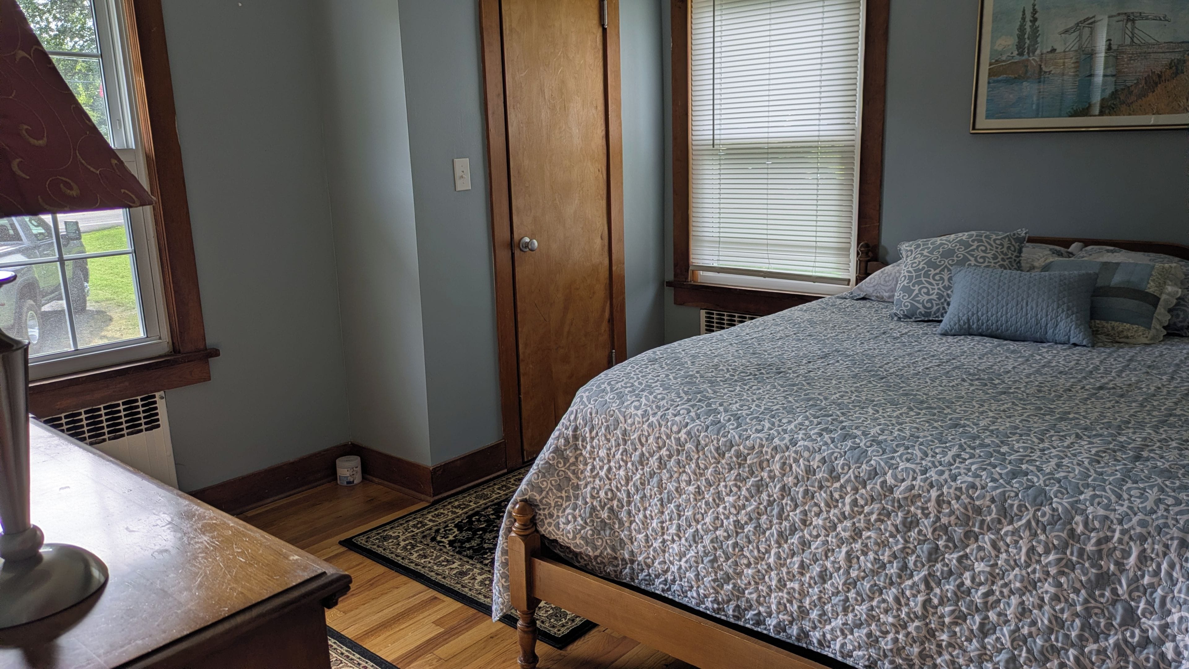 A bedroom with a bed, a wooden door, a window with blinds, and a radiator.