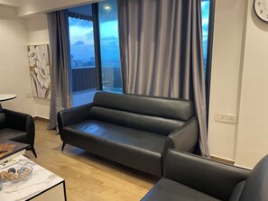 A modern living room with a black leather sofa, a small round table with a bowl of snacks, and a painting on the wall. - Cozy 1-bedroom apartment in beautiful Accra with AC and gym (Accra)