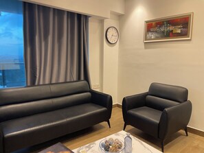 A modern living room with a black leather sofa, a black armchair, a marble coffee table with decorative items, a wall clock, and a framed abstract painting. - Cozy 1-bedroom apartment in beautiful Accra with AC and gym (Accra)