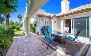 A patio with a table and chairs, a grill, and a view of a garden and building. - Desert Falls Country Club Villa - Remodeled 2BR- Golf, Pickleball, Tennis & Pool (Palm Desert)