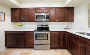 A kitchen with dark wooden cabinets, stainless steel appliances, and a white countertop. - Desert Falls Country Club Villa - Remodeled 2BR- Golf, Pickleball, Tennis & Pool (Palm Desert)