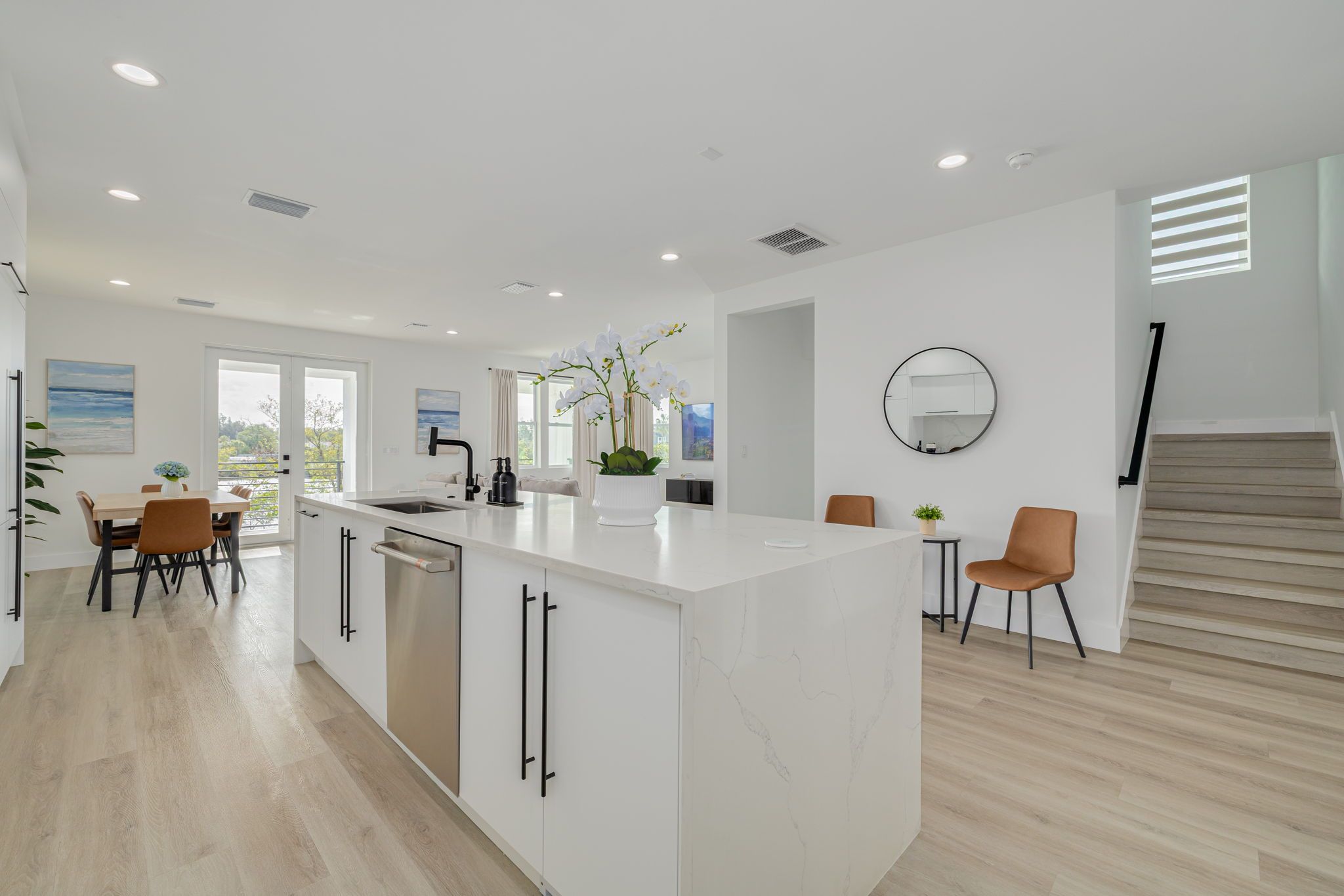 A modern kitchen with a central island, white cabinetry, and a dining area with chairs.