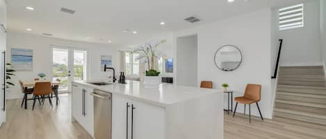A modern kitchen with a central island, white cabinetry, and a dining area with chairs.