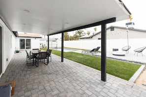 A covered patio area with a brick floor, a table with chairs, and a pool in the background. - Modern Scottsdale/PHX Getaway, Private Heated Pool - Minutes to Golf & Shopping (Phoenix)