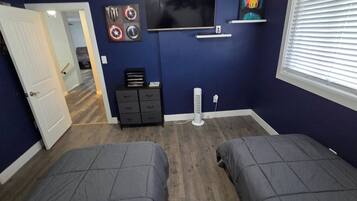 Une chambre avec deux lits, une télévision, une commode et un ventilateur.