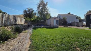 Un jardin avec une clôture en bois, un petit abri de jardin et une maison.