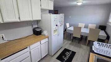 Une cuisine compacte avec des meubles blancs, un réfrigérateur, un grille-pain et un coin repas comprenant une table et des chaises.