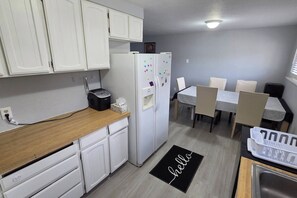 A compact kitchen with white cabinets, a refrigerator, a toaster, and a dining area with a table and chairs. - Entire Upper Floor by ISU • Fenced Yard • Dogs OK (Pocatello)