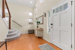 A staircase leading to an upper floor, a white door with a window, a small table with a plant, and a wall-mounted mirror. - Modern 3BR La Jolla Home w/ Panoramic Ocean Views (La Jolla)