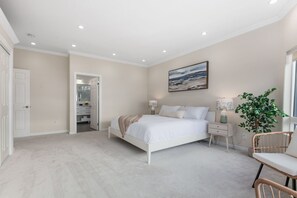 A bedroom with a bed, bedside tables, a nightstand, a chair, a potted plant, and a door leading to a bathroom. - Modern 3BR La Jolla Home w/ Panoramic Ocean Views (La Jolla)