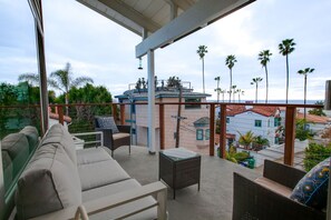 A balcony with outdoor furniture, a view of palm trees, and buildings in the background. - Modern 3BR La Jolla Home w/ Panoramic Ocean Views (La Jolla)