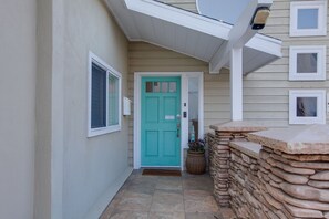 A turquoise door with a small window, a stone wall, and a light fixture above. - Modern 3BR La Jolla Home w/ Panoramic Ocean Views (La Jolla)
