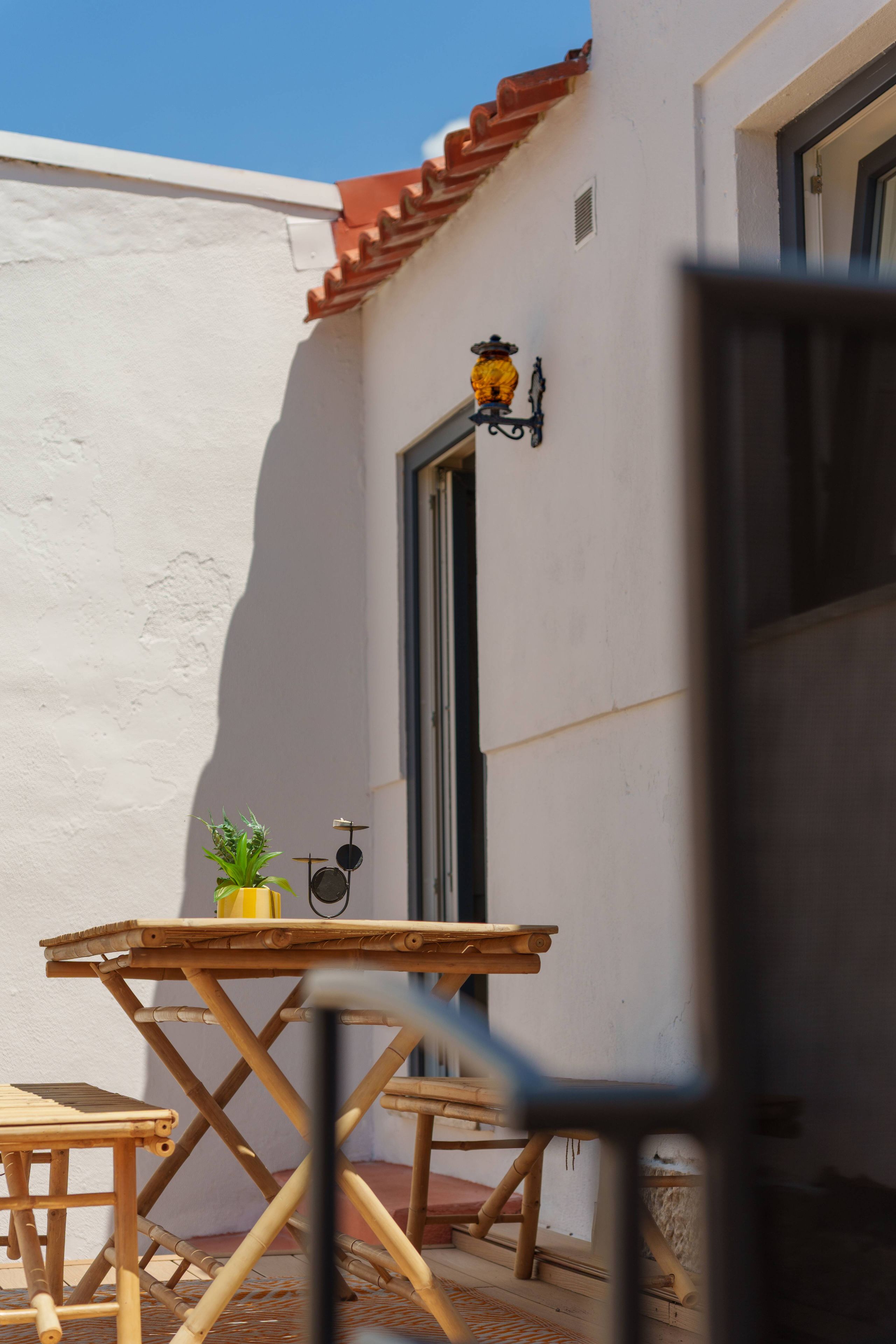 Un petit espace extérieur aménagé avec une table et des chaises, un pot de fleurs et une porte dotée d’une fenêtre.